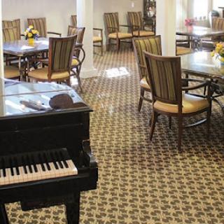 A cozy dining area featuring tables and chairs, with a piano in the foreground.
