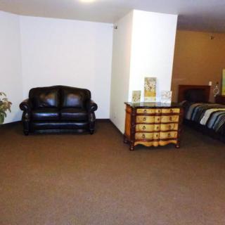 A spacious living area featuring a black leather sofa and a wooden chest of drawers.