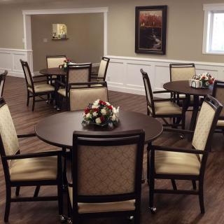 A neatly arranged dining room with round tables and upholstered chairs.