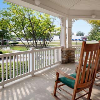 A cozy porch with a wooden rocking chair overlooking a sunny front yard.