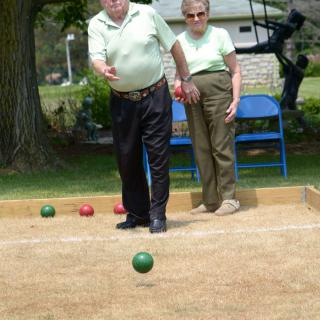 Elderly individuals playing bocce ball outdoors in a park.