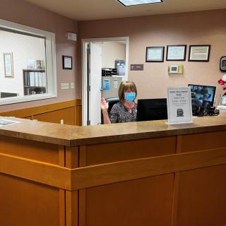 A woman wearing a mask sits at a reception desk in an office setting.