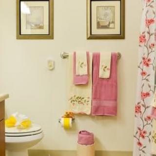 A cozy bathroom with pink and floral decor featuring neatly arranged towels and framed pictures.