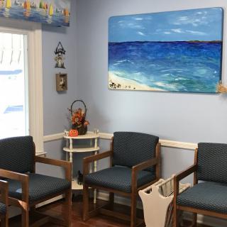 A cozy waiting room with blue walls, decorated with a beach-themed painting and arranged seating.