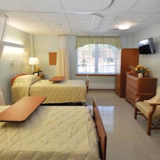 A well-organized hospital room featuring two beds, a dresser, and ample natural light.