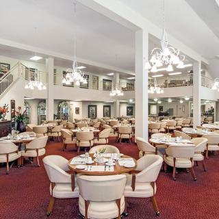 A spacious dining area with elegant chandeliers and neatly arranged tables and chairs.