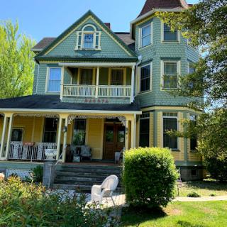 A charming Victorian-style house surrounded by lush greenery on a bright sunny day.