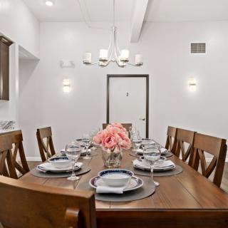 A beautifully set dining table with wooden chairs, elegant dinnerware, and a floral centerpiece under a modern chandelier.
