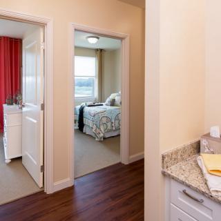 A view of a hallway leading to two bedrooms in a modern apartment.