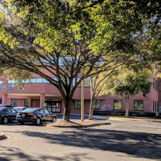 A view of a building surrounded by trees and parked cars in the daytime.