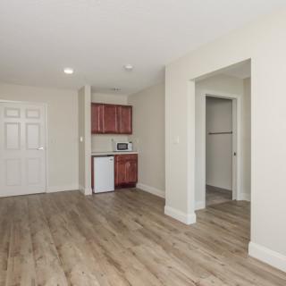 An empty apartment interior featuring a kitchenette and wood flooring.