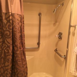 A bathroom with a shower equipped with grab bars and a decorative curtain.