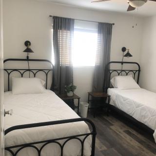 A cozy bedroom featuring two iron-framed beds with white bedding, complemented by wall-mounted lamps and a window with curtains.