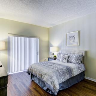 A cozy bedroom featuring a neatly made bed with patterned bedding, two bedside lamps, and hardwood flooring.