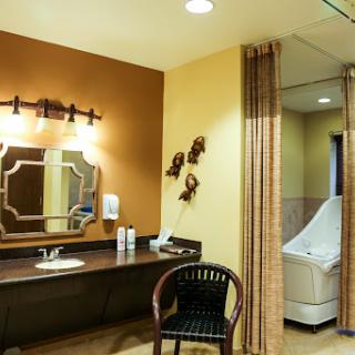 A spacious and well-lit bathroom featuring a vanity area, mirror, and comfortable chair.