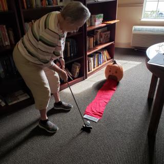 An elderly person playing indoor mini-golf with a pumpkin target.