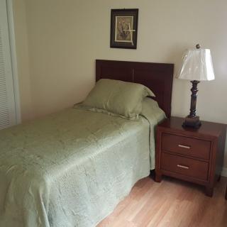 A simple bedroom with a single bed, nightstand, and lamp.