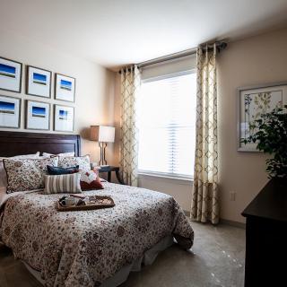 A cozy bedroom with a neatly made bed, artwork on the walls, and soft lighting from a bedside lamp.