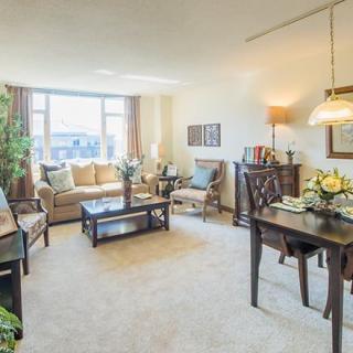 A cozy living room with a comfortable sofa, coffee table, and adjacent dining area, well-lit by natural sunlight.