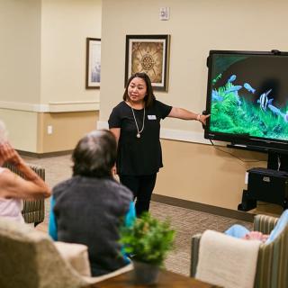 A woman giving a presentation to a small group using a television screen.
