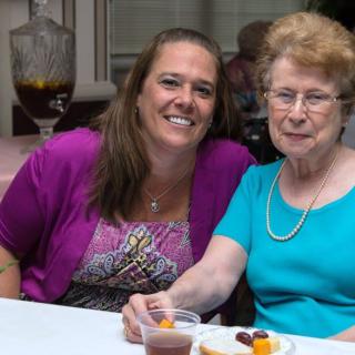 Two women smiling and sitting at a table during an indoor event.