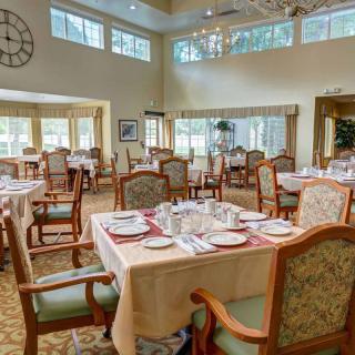 An elegantly set dining room with neatly arranged tables and chairs, featuring large windows and natural light.