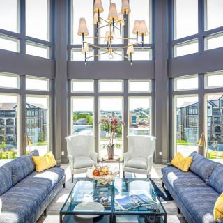 A modern living room with large windows, blue sofas, and a central chandelier.