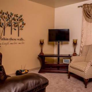 A cozy living room featuring a wall decal with trees, a television on a wooden stand, an armchair, and decorative lamps.