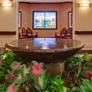 A peaceful indoor lobby featuring a decorative fountain surrounded by vibrant plants and comfortable seating.