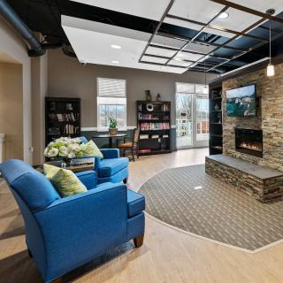 A modern living room with blue chairs, a stone fireplace, and a wall-mounted television.