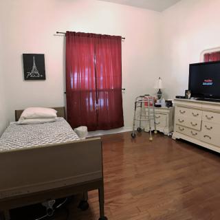 A bedroom with a hospital bed, dresser, TV, and red curtains.