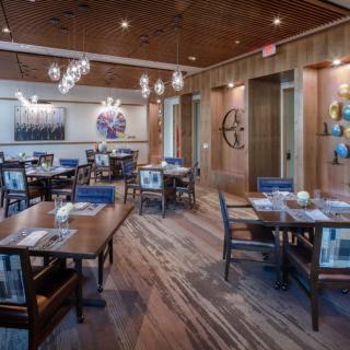 A modern restaurant interior with neatly arranged tables and chairs, featuring stylish lighting and wood flooring.