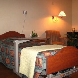 A cozy patient room featuring a bed with a blanket, a chair, and warm lighting.