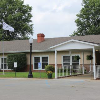 A welcoming entrance of a residential institution with a flag and landscaped surroundings.