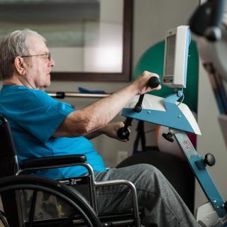 An elderly person exercising on a rehabilitation machine while seated in a wheelchair.