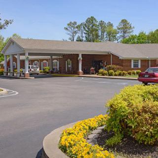 A single-story building with a covered entrance, surrounded by a parking lot and landscaped with flowers and shrubs.