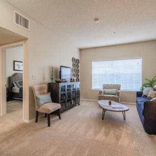 A cozy living room with modern decor, featuring a sofa, chairs, coffee table, and a television in front of a large window.