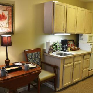 A cozy kitchenette with a small table and chairs, cabinets, and a lamp.