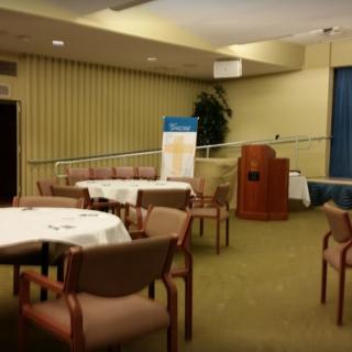 An empty conference room with tables and chairs arranged, featuring a podium at the front.