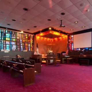 A church interior with stained glass windows, rows of pews, and vibrant lighting.