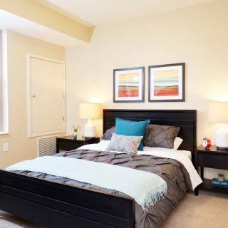 A modern bedroom with a neatly made bed, accented by colorful artwork and matching lamps on nightstands.
