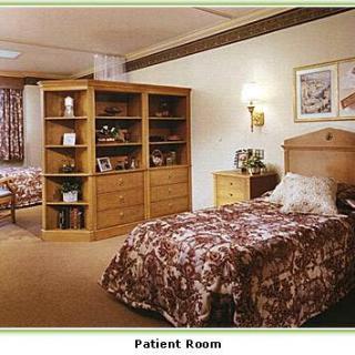 A cozy patient room with two beds, wooden furniture, and decorative elements.