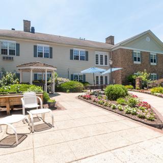 A charming building with a well-maintained garden and outdoor patio seating on a sunny day.