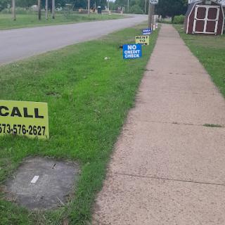 A view of a sidewalk lined with various advertising signs, showcasing businesses along the road.