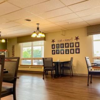 A cozy dining area with neatly arranged tables and chairs, illuminated by warm ceiling lights, featuring decorative elements on the walls.