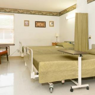 A well-equipped hospital room with two beds, a table, and a privacy curtain.