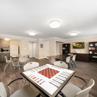 A modern living space featuring a chessboard on a table, surrounded by chairs with an adjacent kitchen area.