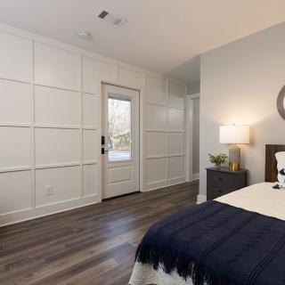 A contemporary bedroom with white paneled walls, dark wood flooring, and modern decor.