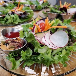 A fresh mixed green salad with radishes, carrots, and almonds served on a glass plate.