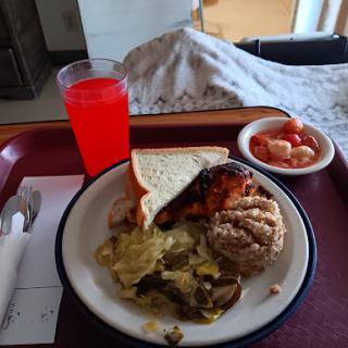 A hospital meal featuring a variety of foods including a sandwich, mixed vegetables, fried chicken, and a colorful beverage.